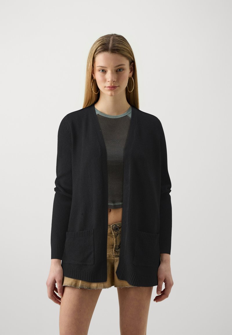 Svart cardigan med V-hals-design, som har to frontlommer og ribbet kant. Matchet med en cropped topp og denimshorts.