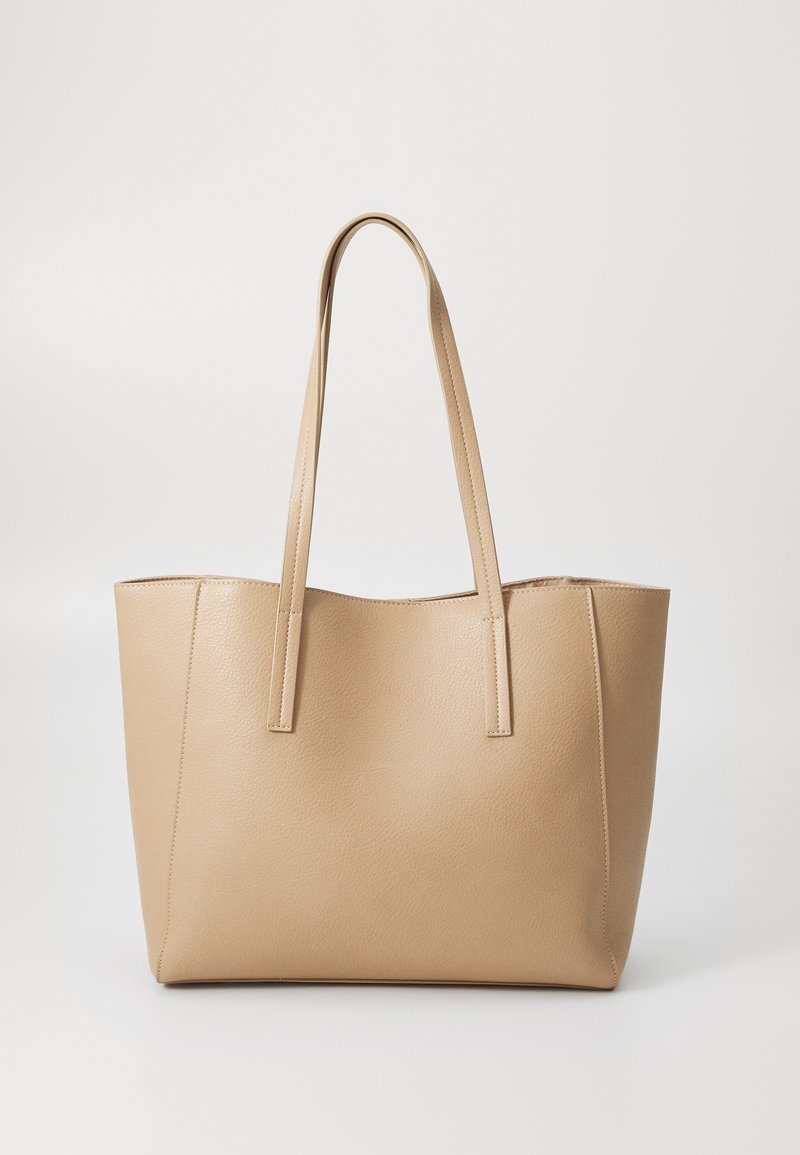 Sac fourre-tout en cuir beige avec deux longues poignées, de forme rectangulaire, surface texturée et un minimum de détails de couture. Aucune fermeture visible.