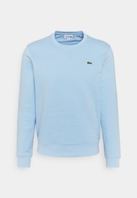 Ljusblå sweatshirt med långa ärmar, rund halsringning, mjuk textur och en liten grön krokodil-logotyp på bröstet. Enkel, klassisk design.