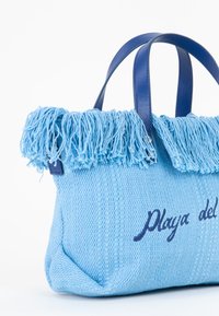 Borsa tessuta di colore azzurro chiaro con una parte superiore frangiata, manici blu navy e testo ricamato "Playa del" in blu scuro. Tessuto con texture.