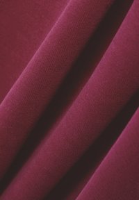 Tessuto di un profondo bordeaux con una consistenza morbida e liscia e una leggera lucentezza, che presenta pieghe delicate e un motivo a maglia uniforme.