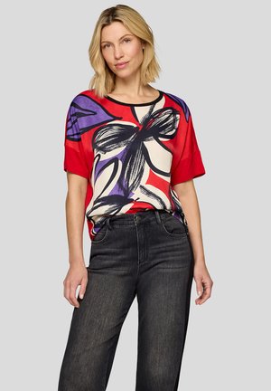 Rotes und cremefarbenes Hemd mit schwarzen und lila Blumenmustern, kurzen Ärmeln, rundem Ausschnitt, kombiniert mit dunkelgrauen, hoch taillierten Jeans.