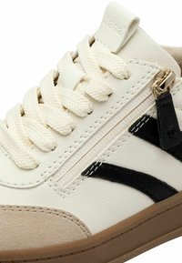 Baskets en cuir crème avec des accents noirs, en suède beige texturé, cordons blancs et une fermeture éclair sur le côté avec un tirette métallique.
