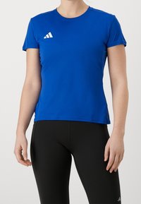 Kvinna iförd en blå kortärmad träningströja och svarta leggings med vita logotryck på bröstet och låret.