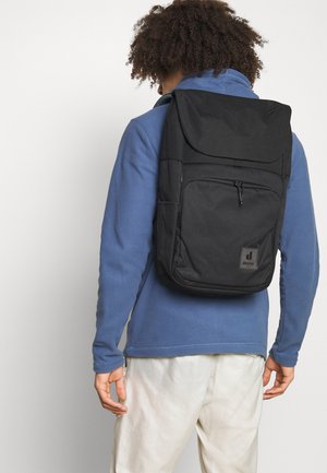 Schwarzer Rucksack mit Klappenverschluss, vorderer Reißverschlusstasche und Markenlogo. Hergestellt aus strapazierfähigem Stoff, ausgestattet mit gepolsterten Trägern und einem strukturierten Design.