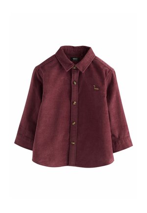Cămașă din corduroy maron cu mâneci lungi, guler ascuțit, închidere cu nasturi în față și un logo mic brodat pe piept. Material texturat.
