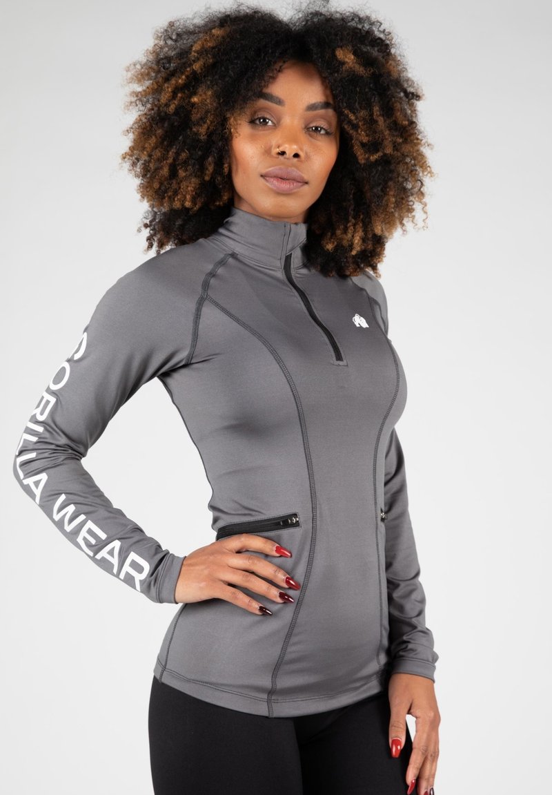 Grijze langemouwen kwart-rits top van rekbaar materiaal, met ritssluitingen aan de zijkant en gedurfde witte branding op de mouwen.
