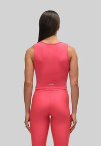 Rosa sportstopp i cropped design, med slät yta, ärmlös skärning och logotypdetalj på baksidan, matchad med åtsittande leggings.