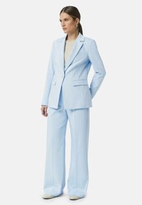 Lichtblauw op maat gemaakt pak met gestructureerde blazer, notch-lapels en twee voorzakken. Brede broekspijpen, gladde textuur, moderne fit.