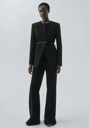 Black tailored suit with a fitted blazer and wide-leg trousers. Smooth fabric with a minimalist design and a thin, metallic waistbelt.