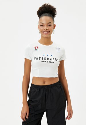 Valkoinen lyhythihainen t-paita, jossa lukee mustalla "UNSTOPPABLE WORLD TEAM", punainen numero "17" ja sinisiä tähtiä. Yhdistetty mustiin löysiin housuihin.
