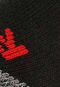 Tejido negro con un patrón de punto texturizado que presenta un logotipo bordado en rojo. Se aprecian toques de gris en la sección inferior.