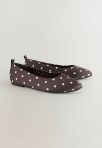 Schwarze Ballerinas mit weißen Punkten, mit abgerundetem Zeh und einer niedrigen, flachen Sohle. Das Innere zeigt ein dezentes Tupfenmuster.