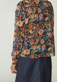 Blommig blus med långa ärmar med orange, rosa och blå blommor, bärs med mörk denimkjol, visar ryggvy av personen.