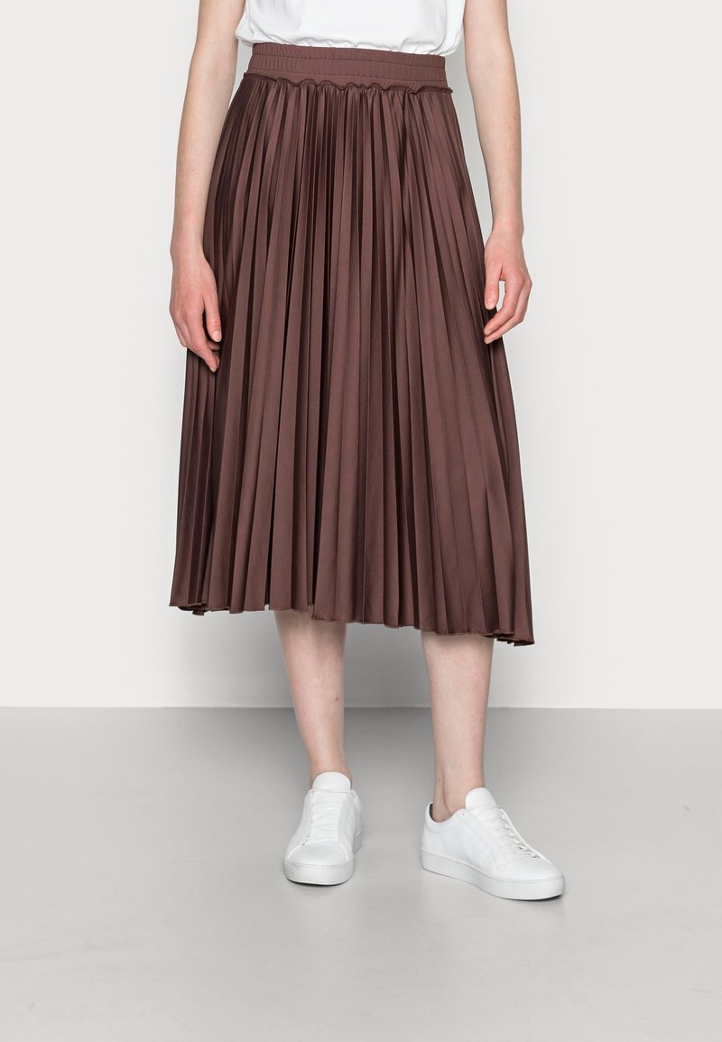 Fållad midijupe i brun tyg med elastisk midja, bärs med vita sneakers. Kjolen har en flödig design och mjuk textur.
