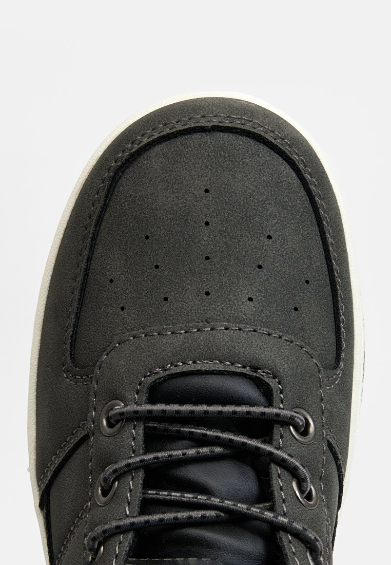 Szare skórzane trampki z zaokrąglonym noskiem, perforowanym wierzchem i kontrastującymi czarnymi sznurowadłami. Biała gumowa podeszwa i przeszycia wokół krawędzi.