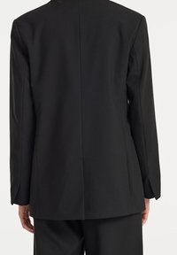 Černý upravený blejzr s dlouhými rukávy, hladkou texturou látky, strukturovaným střihem a jedním detailem rozparku na zadní straně.