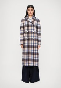 Manteau à carreaux dans des tons de marron, beige et bleu. Design croisé avec des boutons en argent, grandes poches et manches longues.