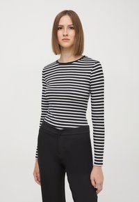 Maglietta a maniche lunghe a righe bianche e nere con scollatura tonda, abbinata a pantaloni neri aderenti. Tessuto morbido, vestibilità slim e design minimale.