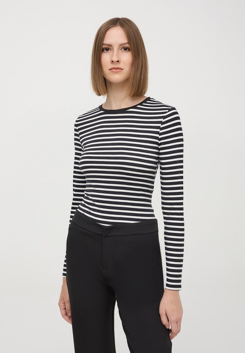 Maglietta a maniche lunghe a righe bianche e nere con scollatura tonda, abbinata a pantaloni neri aderenti. Tessuto morbido, vestibilità slim e design minimale.