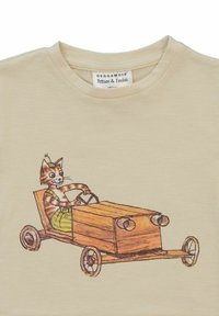 Vaalea beige t-paita, jossa on graafinen kuva raidallisesta kissasta, joka ajaa puuautoa, jossa on pyöreät ajovalot ja mustat renkaat.