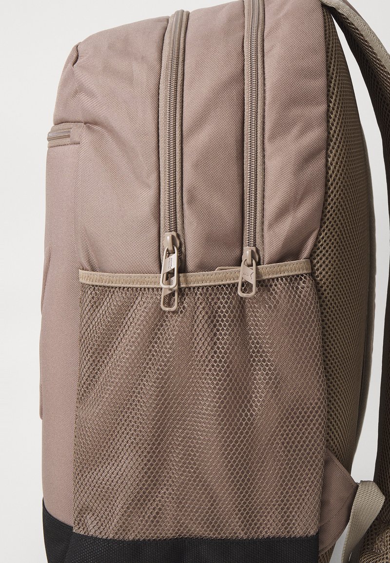 Zaino in tessuto marrone con due scomparti con zip e una tasca laterale in rete. Presenta un design resistente e una chiusura lampo liscia.