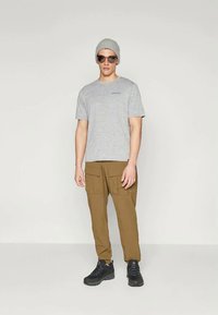 Pilkas trumpas rankovėmis marškinėliai su mažu logo, rudos kargo kelnės su šoninėmis kišenėmis, pilka skrybėlė ir juodi sportbačiai.