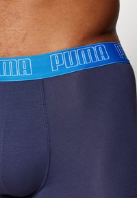 Marinefarbene Boxershorts mit blauer elastischer Taille, die das weiße "PUMA"-Logo zeigt. Weicher Stoff mit glatter Oberfläche und genähten Nähten.
