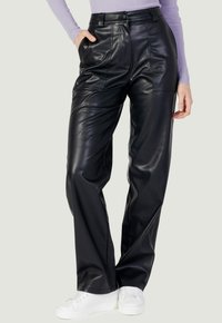 Zwarte neplederen broek met hoge taille, voorzakken en een ontspannen pasvorm. Gladde textuur en glanzende afwerking. Gestyled met witte sneakers.