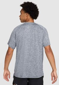 Camisa atlética de manga corta para hombre en tejido gris jaspeado. Presenta un cuello redondo, mangas raglán y un dobladillo trasero ligeramente más largo para mayor comodidad.