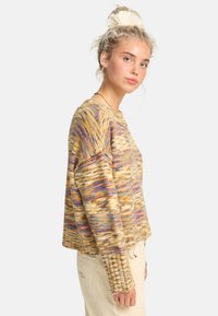 Sweter dzianinowy w kolorze żółtym z wielokolorowymi wzorami, charakteryzujący się luźnym krojem, okrągłym dekoltem i ściągaczami. Teksturowany, ciepły materiał.