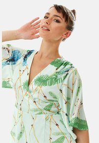 Light green dress with a deep V-neck, short sleeves, and an all-over palm and bird print. Smooth fabric with a flowing cut.