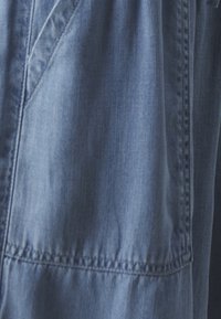 Svetle modrá denimová tkanina s hladkým povrchem, se zřetelným švem a detailem s nařaseným švem. Neformální design se softovými záhyby.