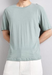T-shirt vert clair à manches courtes en tissu doux, avec un col rond et une coupe décontractée. Design uni sans motifs visibles.