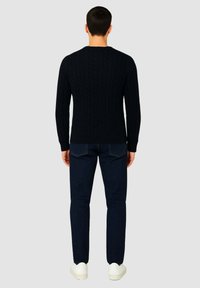 Maglione navy a maglia intrecciata con polsini e orlo a coste, abbinato a jeans scuri e sneakers bianche, visto da dietro.