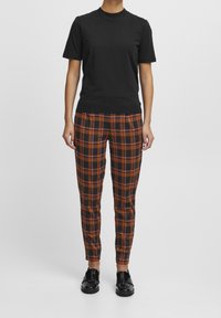 Black short-sleeve t-shirt paired with fitted plaid trousers in orange, black, and white, featuring a smooth texture and a streamlined design.