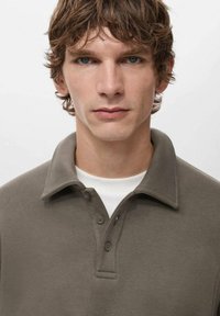 Graues Poloshirt mit einem Kragen und einer Knopfleiste mit drei Knöpfen. Der Stoff wirkt glatt und weich und bietet eine figurbetonte Passform.