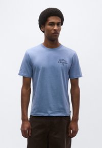 Ανοιχτό μπλε βαμβακερό μπλουζάκι με κοντά μανίκια, στρογγυλή λαιμόκοψη και λογότυπο στο στήθος που γράφει "SCOTCH & SODA CO." Το κείμενο είναι σε σκούρο μπλε χρώμα.