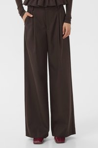 Wide-leg trousers in dark brown fabric with a smooth texture, featuring pleats and side pockets. Styled with a layered top and burgundy shoes.