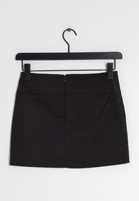 Jupe mini noire avec détail de rayure latérale suspendue sur un cintre noir, contre un fond blanc.