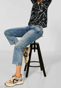 Svart skjorta med vitt abstrakt mönster, ljusblå cropped jeans med fransad fåll och beige sneakers med orange och marinblå detaljer.