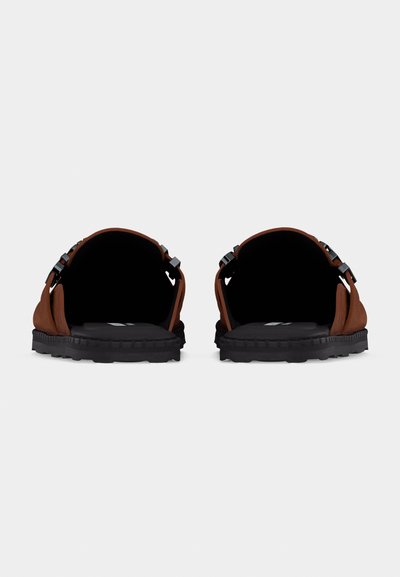 Sandales marron à talons ouverts avec semelles noires et brides latérales réglables, vues de l'arrière sur un fond clair uni.