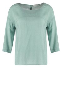 Blouse vert clair à manches longues avec un petit motif à pois blancs et un col rond avec une petite fermeture par bouton dans le dos.