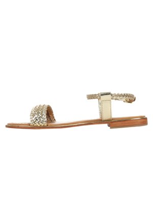 Sandales en métal tissé doré avec une semelle en bois plate et une sangle à la cheville, présentant un design tressé sur l'orteil et une boucle ajustable.