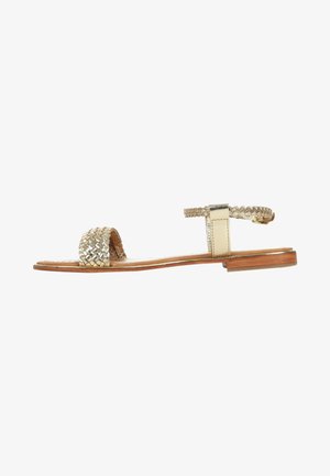 Sandales en métal tissé doré avec une semelle en bois plate et une sangle à la cheville, présentant un design tressé sur l'orteil et une boucle ajustable.