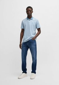 Polo shirt azzurro chiaro con colletto discreto, abbinato a jeans blu scuro e sneakers bianche, che mostrano una vestibilità rilassata e uno stile informale.