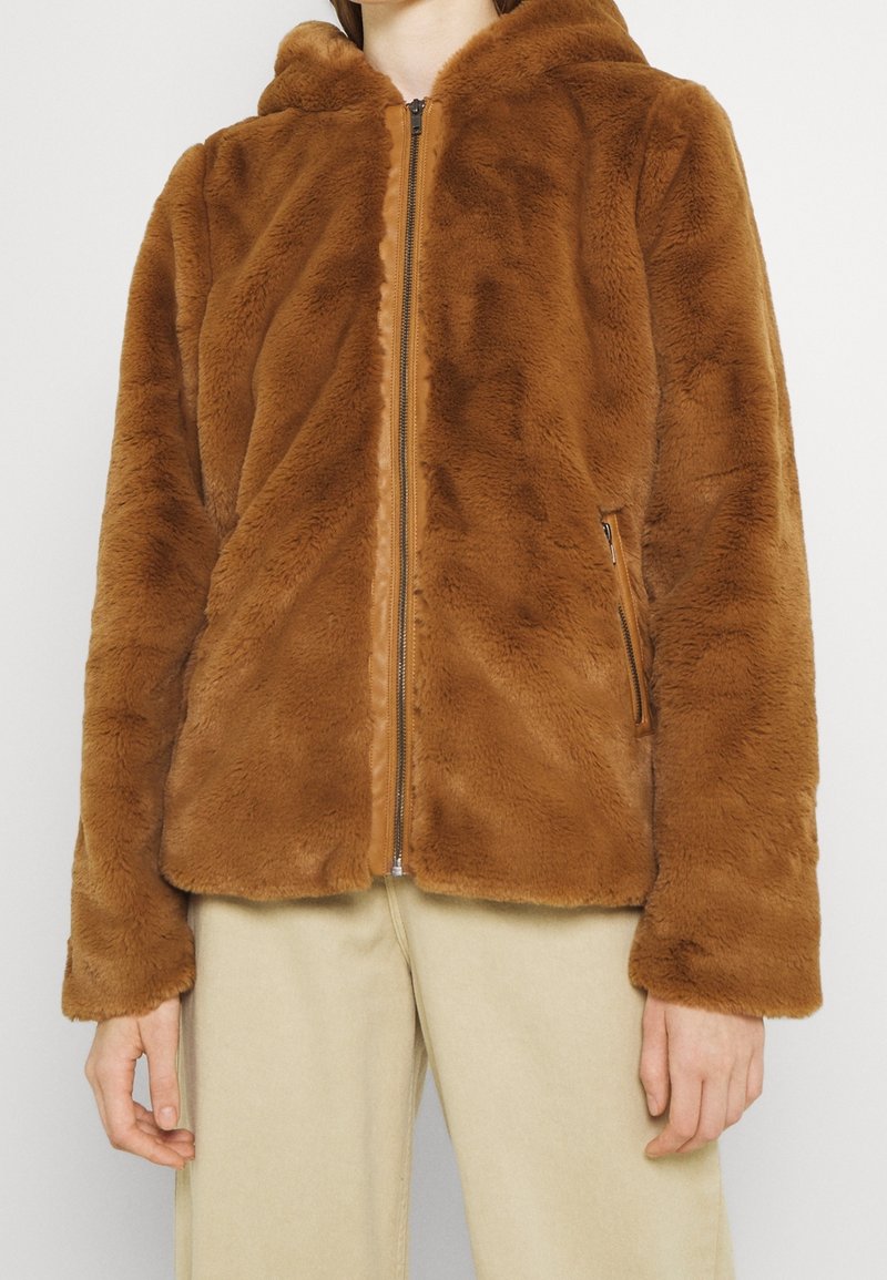 Veste en fausse fourrure marron zippée avec capuche, dotée d'une doublure lisse et de poches latérales. La texture est douce et moelleuse.