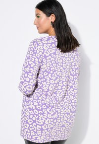 Fioletowa bluzka z leopardzim wzorem i długim rękawem, wykonana z miękkiego materiału, charakteryzująca się luźnym krojem i okrągłym dekoltem z kontrastującymi kremowymi wzorami.