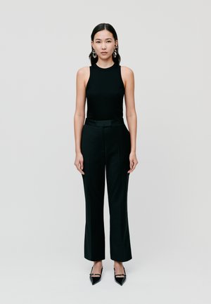 Black sleeveless top paired with high-waisted black trousers. Glossy black pointed-toe shoes with ankle strap, silver hoop earrings visible.
