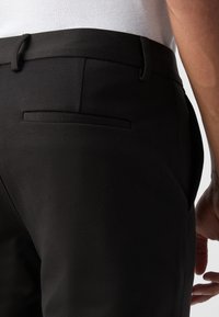Sorte bukser med en glat tekstur, slim fit og en enkelt baglomme med et elegant design detail ved taljen.